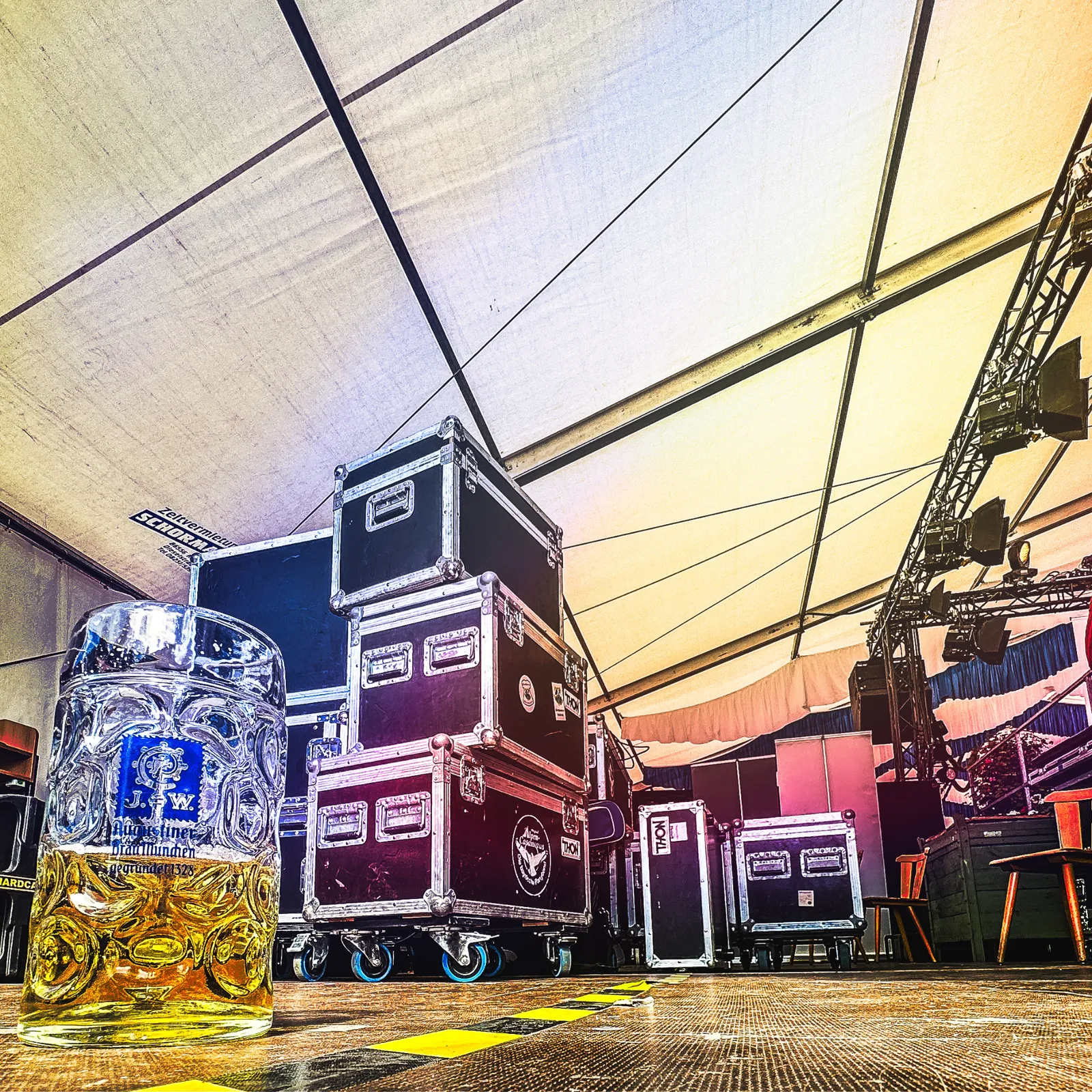 Bierkrug und Flightcases neben einer Festzeltbühne